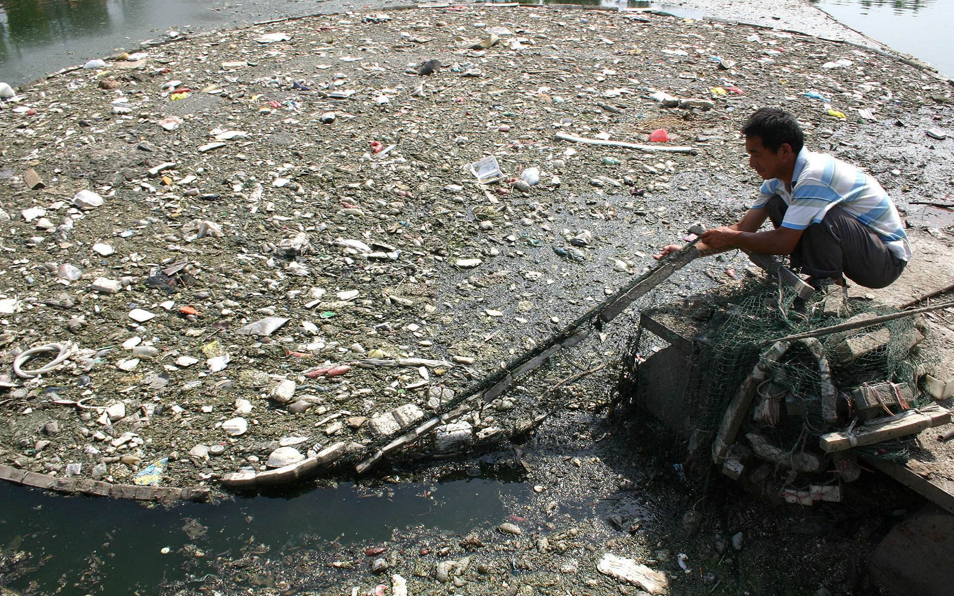 一个中国人正在北京的某条运河上清理河面垃圾。/AP