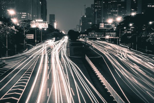 Time-lapse photograph of Shenzhen at night transforms cars into streaks of light passing below illuminated road signs and towering office buildings.