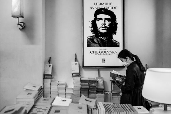 A ponytailed customer in a surgical face mask browses a selection of books below a poster of Che Guevara.