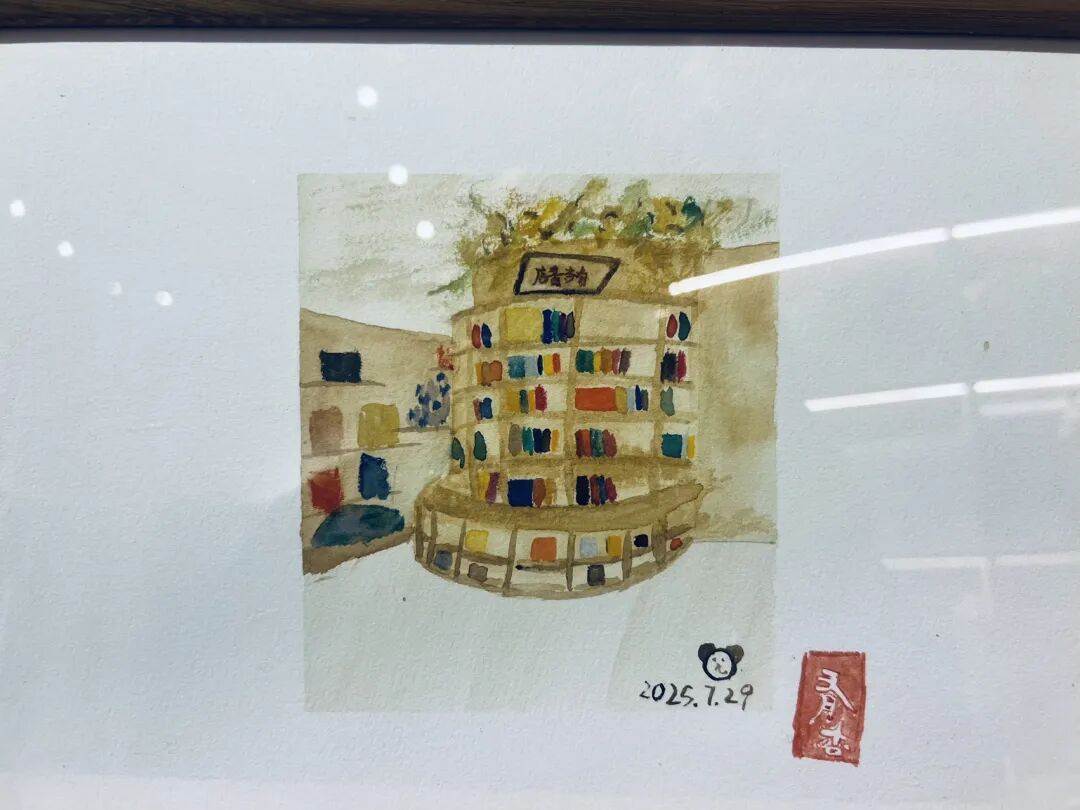 A watercolor of the bookstore’s curved shelves, filled with books, in tones of white, tan, brown, blue, red, yellow, and other colors. In the bottom right-hand corner is a cute face with Mickey Mouse ears, the date July 27, 2025, and the impression of a red seal with Chinese characters that read “You Xing.” 
