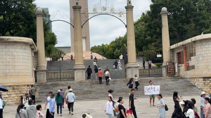 A man holding a sign saying "Xi Jinping must go!" in front of the steps to a large public memorial