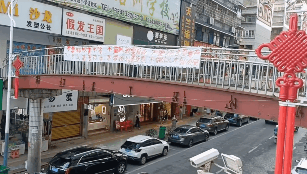 A banner hanging from a pedestrian bridge: “We want equality, not privilege; freedom, not risk control. We want dignity, not lies; reform, not Cultural Revolution. We want elections, not rulers. Be citizens, not slaves.”