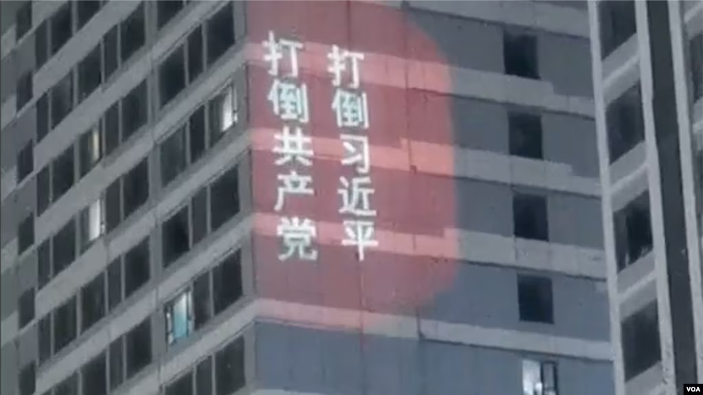 "Down with Xi Jinping! Down with the Communist Party!" is projected onto the side of a building in white characters on red