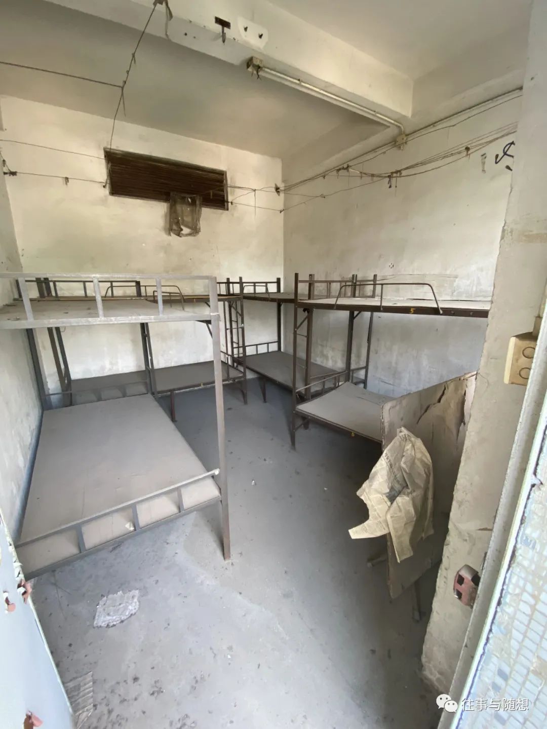An abandoned dormitory room with four metal bunk beds, concrete walls and concrete floors.
