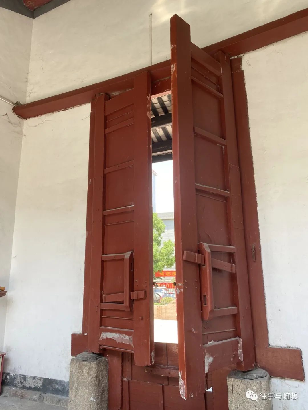 A very tall, red Chinese style wooden door, set into a white wall