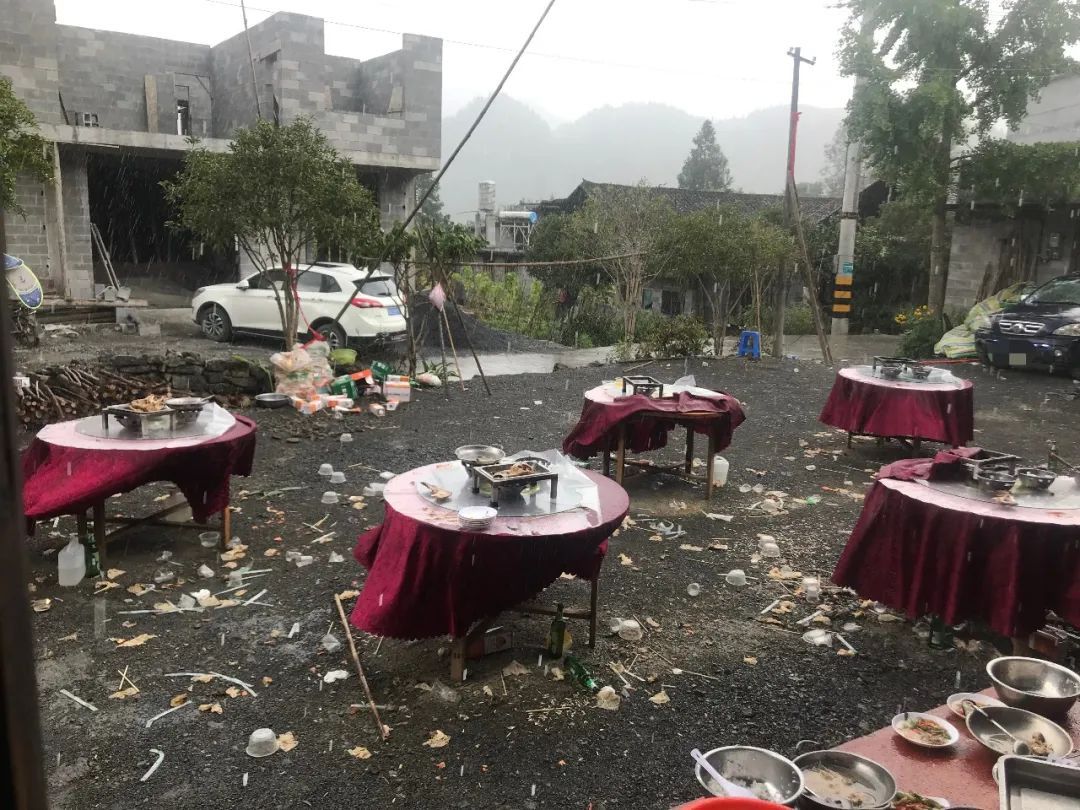 Five round banquet tables stand abandoned: serving dishes and bowls litter their surfaces, and the ground is strewn with debris.