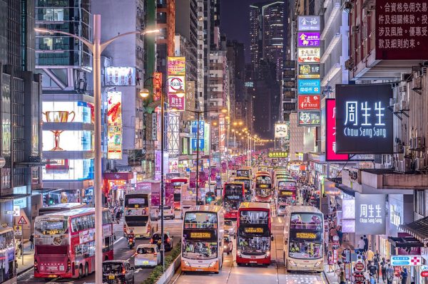 Brilliantly colored neon signs and enormous television screens illuminate a street crowded with cars, double-decker buses, passersby and high-rise buildings in Mong Kok, Hong Kong.