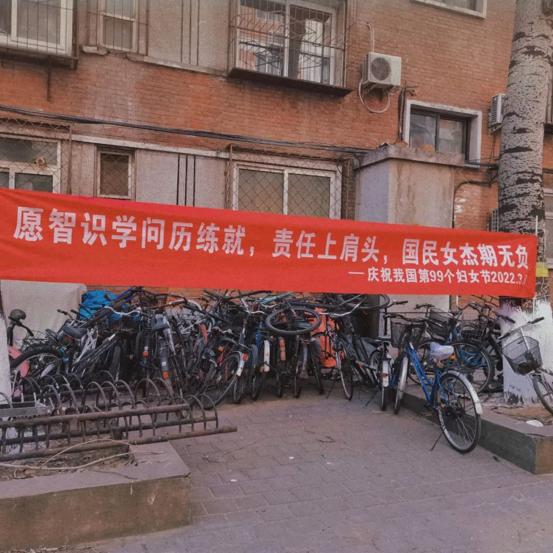 A red and white banner hung above a heap of bikes and bike racks offers best wishes to “national heroines” on International Women’s Day.