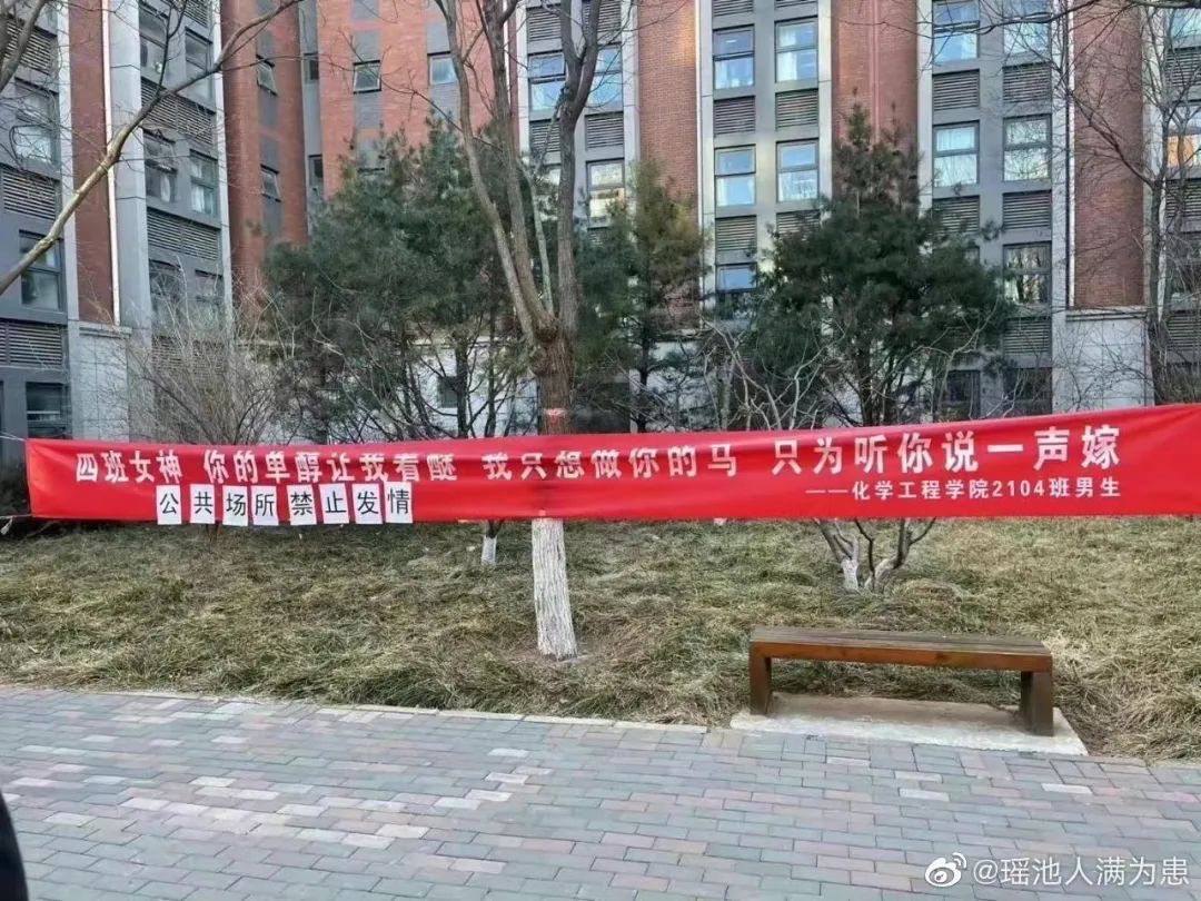 A red banner strung from trees along a walking path near a campus dormitory uses suggestive language to communicate a message from male classmates to their female classmates. Someone has attached a rebuttal to the banner using individual sheets of white paper.