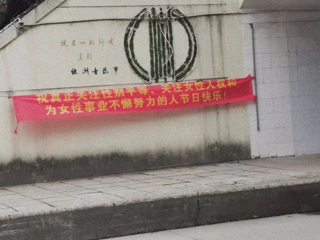 This red banner with yellow text hangs below some wall graffiti next to an underpass.