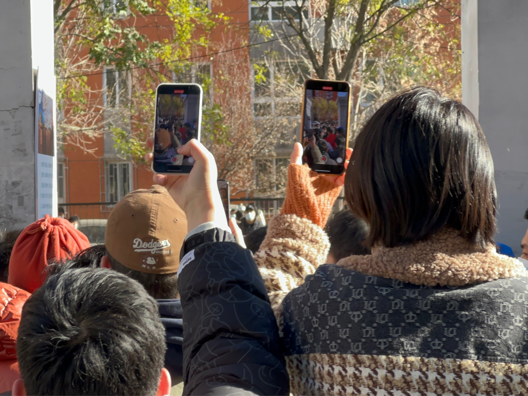 Two young people, seen from behind, are recording the events on their cell phones.