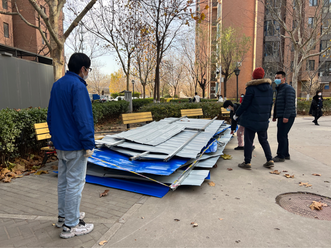 A few residents stand around a thigh-high pile of panels, remnants of the dismantled sheet-metal fence, that have pushed to the side of the pavement near several benches.
