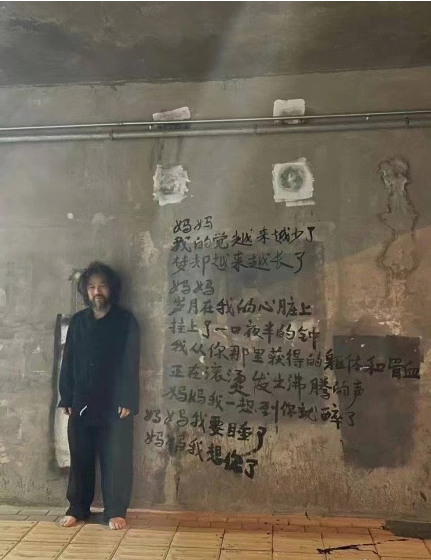 Zhang Boyi posing alongside his poem written on the wall of an underpass. 