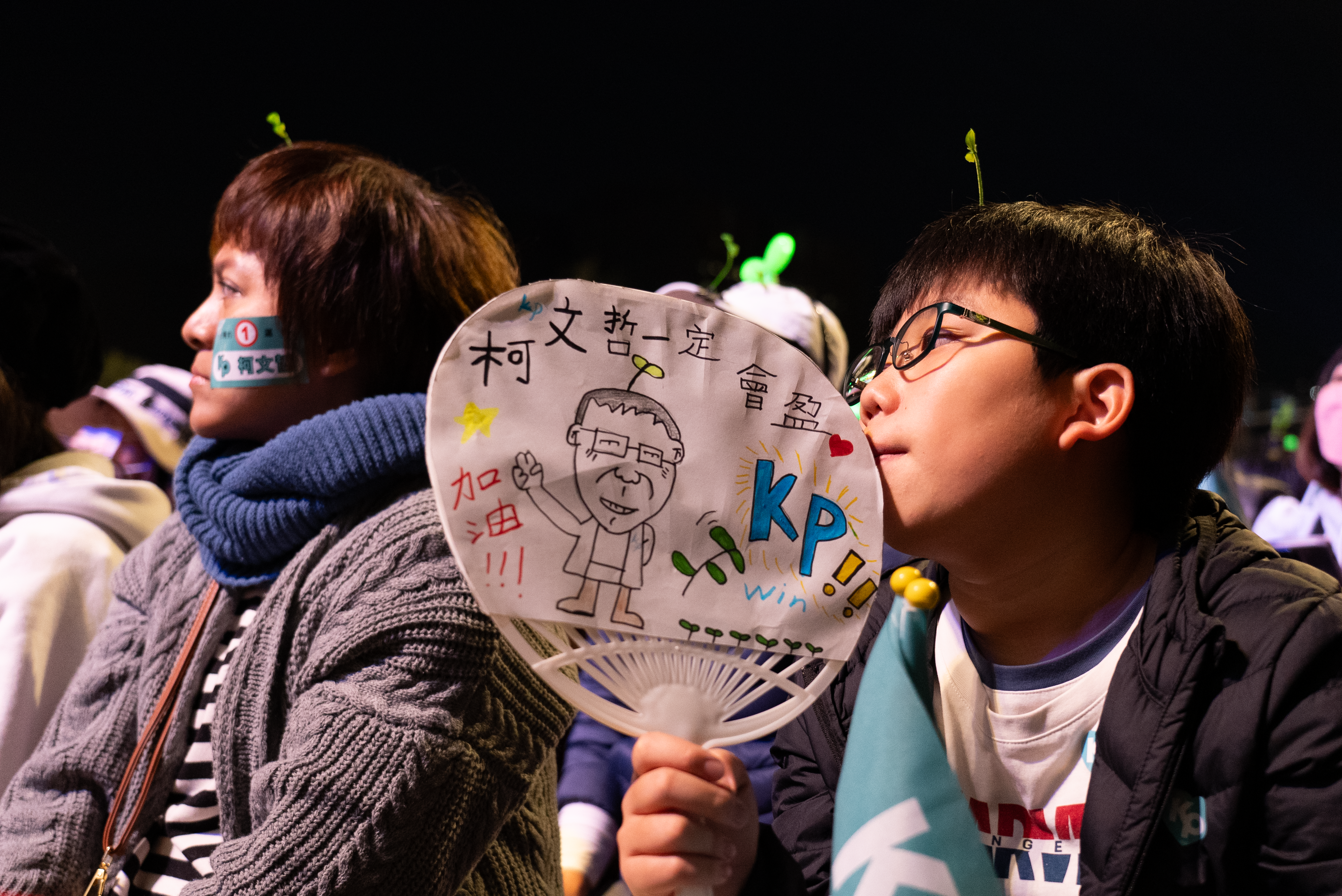 一个小男孩手持一把扇子，以表达对于柯文哲竞选团队的支持。