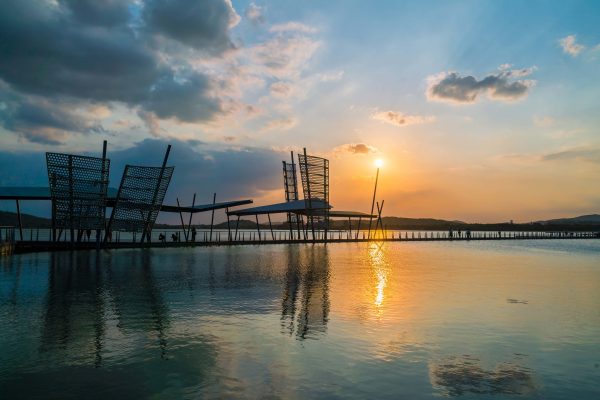 Decorative metal scaffolding, seen in silhouette against a turquoise sky and yellow setting sun, adorns a pier in the city of Wuxi, in China’s Jiangsu Province.