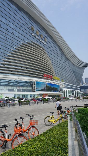 Parked cars and red and yellow rental bikes are dwarfed by the enormous glass and white metal facade of the New Century Global Center, a 1.7 million square meter shopping and entertainment complex in the metropolis of Chengdu, Sichuan Province.