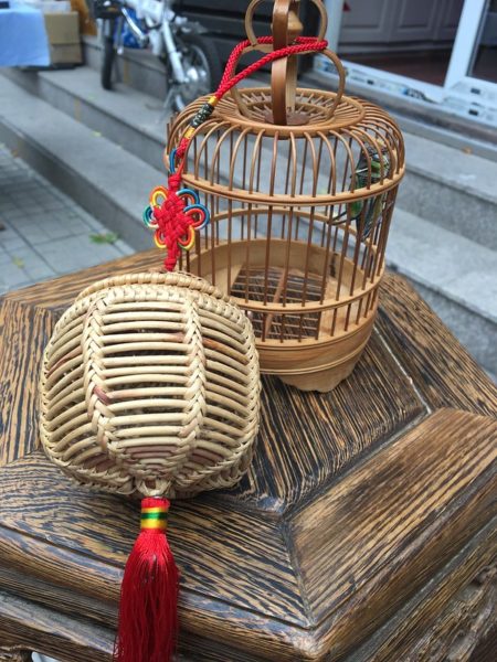 Two wooden cricket cages decorated with traditional red silk knots adorn a small, hexagonal wooden table. 