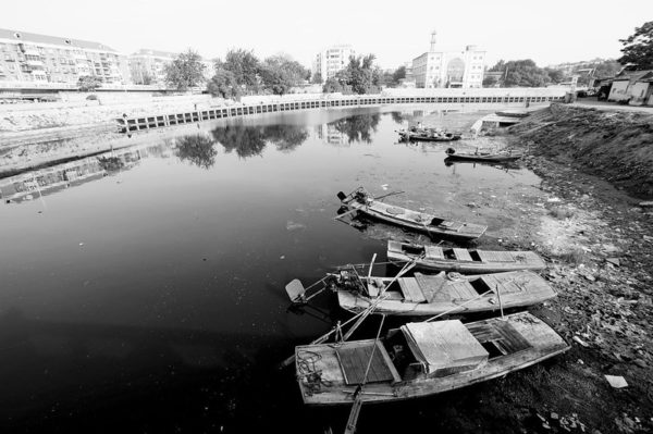 Pale panorama of wooden fishing boats along the Beiyunhe, the northern leg of the former Tianjin-to-Beijing Grand Canal, now lined with multi-story buildings.