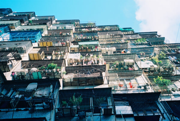 Viewed from below, the barred windows of a high-rise apartment building look like a collection of metal cages filled with plants, clothing and other sundries.