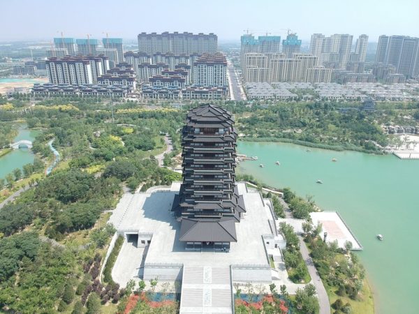 A large, traditional-style but recently built tower in a wetland park with ranks of modern houses and apartment blocks in the background