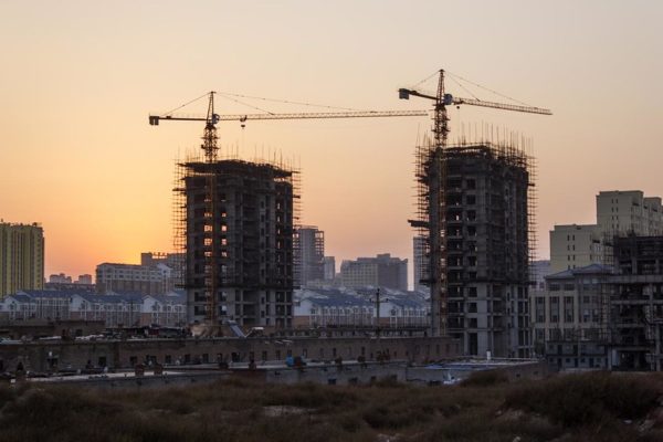 Silhouetted by the setting sun, two enormous cranes perch atop a pair of high-rise buildings under construction in a modern city in Inner Mongolia, China.