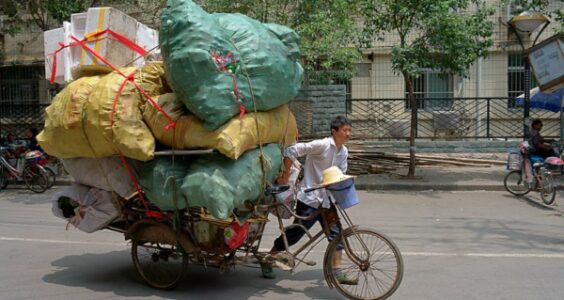 A man pushing a heavily overloaded tricycle