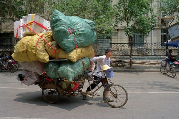 A man pushing a heavily overloaded tricycle