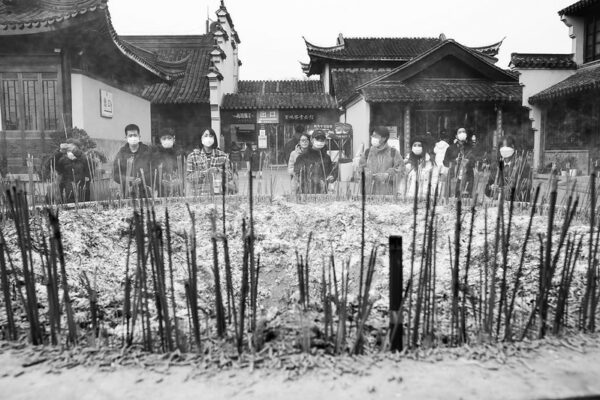 Masked people burn incense sticks around a large round basin with traditional Chinese buildings in the background