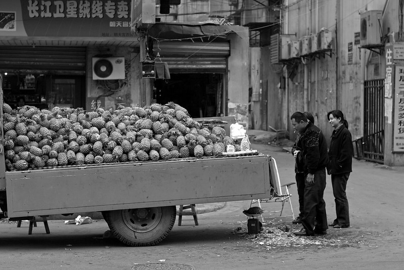 A man selling pineapples piled on the back of a truck weighs one for a customer