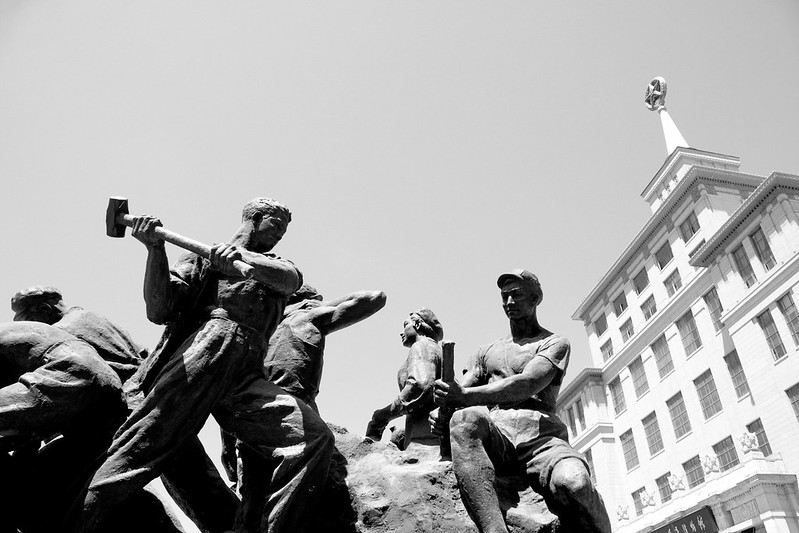 Viewed from below, this vintage socialist-style statue shows workers emerging from the metal they were forged from.