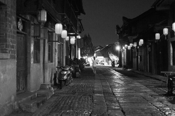 Lanterns hung from the eaves of traditional tile-roofed buildings light the way down this narrow cobblestone street.