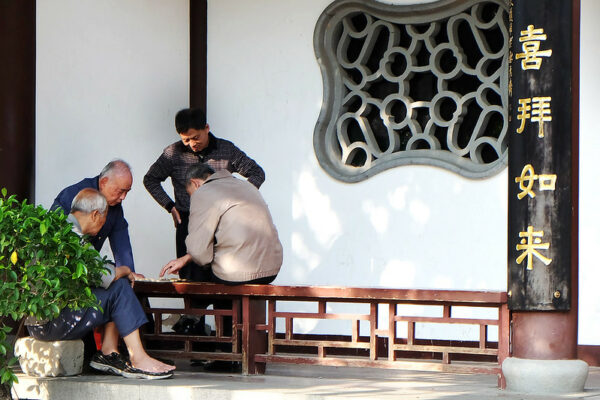 Four men - two playing, and two watching - are immersed in a game of Chinese chess in an ornamental passageway in Fuzhou’s scenic West Lake Park. The scene is friendly and casual, and one man has removed one of his tennis shoes.
