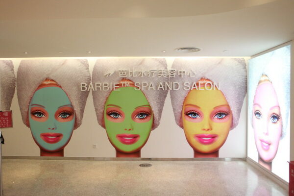 A wall display for a Barbie-themed beauty spa in Shanghai features several images of the iconic doll with a white towel on her head and aqua, green, and yellow facial masks.