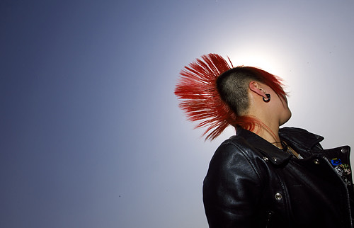 Against a clear blue sky, a side view of a 2006 Midi Music Festival concertgoer with a black leather jacket, silver earring, and enormous red mohawk.
