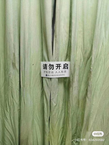 Screenshot of a pale green curtain affixed with a black and white sign.
