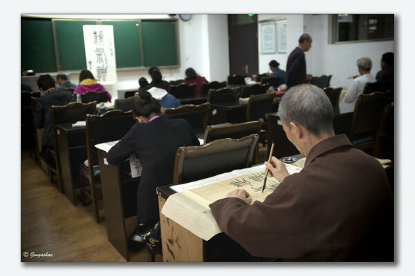 A classroom full of students, ranging from young adults to much older people, practice their calligraphy at a school in Chengdu, Sichuan.