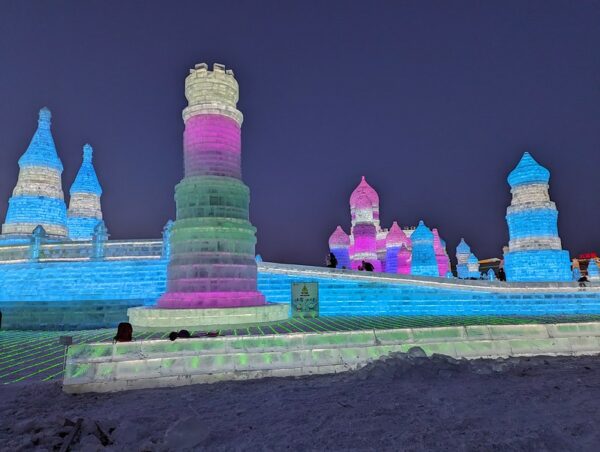 Architectural ice sculptures in the shape of towers, turrets, and onion domes are made from blocks of ice that appear to be illuminated from within with blue, white, green, pink, and purple lights.