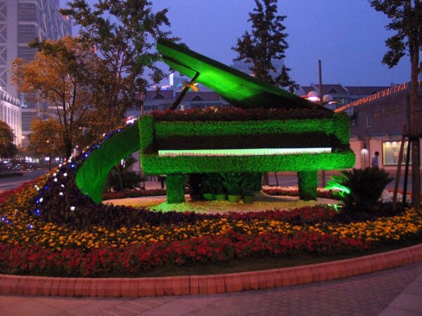 A topiary sculpture shaped like a giant grand piano and surrounded by a semicircle of flowers adorns a small park in Shanghai.