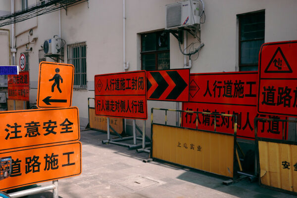 A collection of red, orange, and yellow street signs in Shanghai caution about road work and pedestrian safety.