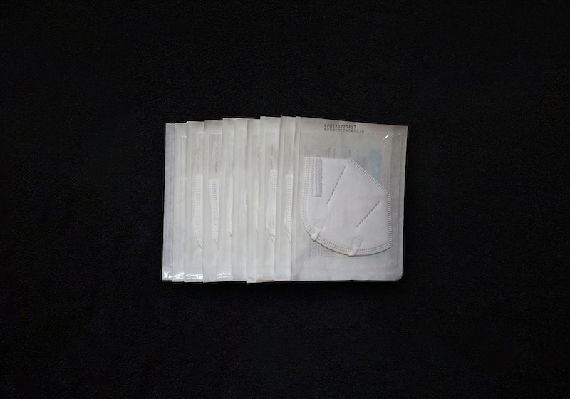 Ten white N95 masks, each wrapped in a clear plastic package, against a black backdrop