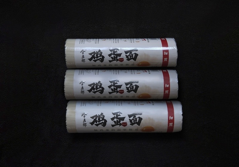 Three cylindrical packages of egg noodles with labels in red, black, and white.
