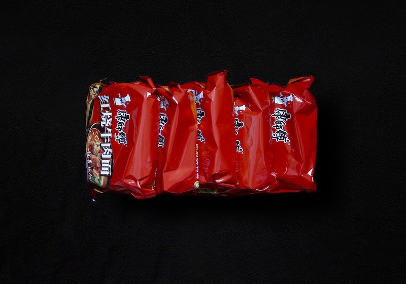 Five bright-red packets of instant noodles against a black background.