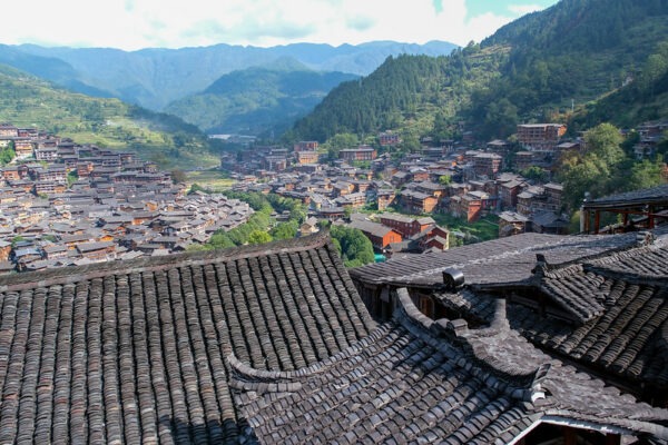 Charming traditional architecture—low gray, orange, and red buildings with slate-gray tiled rooftops—graces the township of Xijiang, set amid the deep green forested hills of Leishan county, Guizhou province.